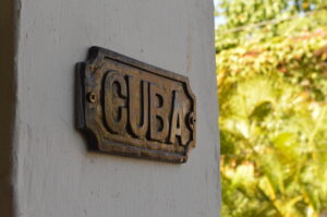 The Scenic & Cultivated metal sign is mounted on a white wall, with greenery and sunlight softly blurred in the background. | Cubaecology