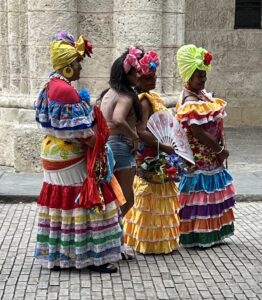 Four women pose outdoors by a stone wall—three in colorful ruffled dresses and headwraps from Scenic & Cultivated, and one in casual wear. | Cubaecology